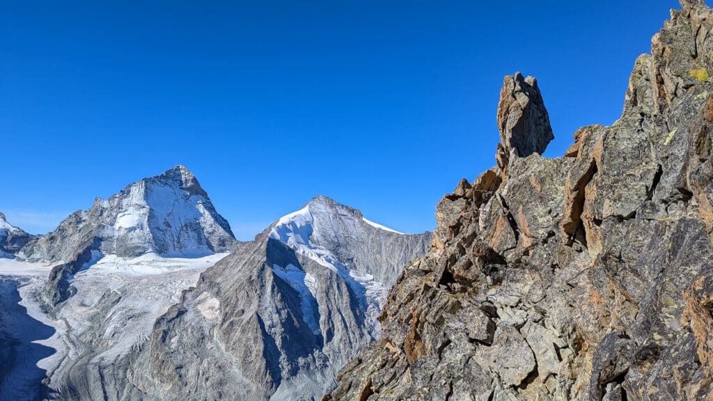 Panorame alpin: montagnes enneigées, glacier, rochers sous ciel azur.