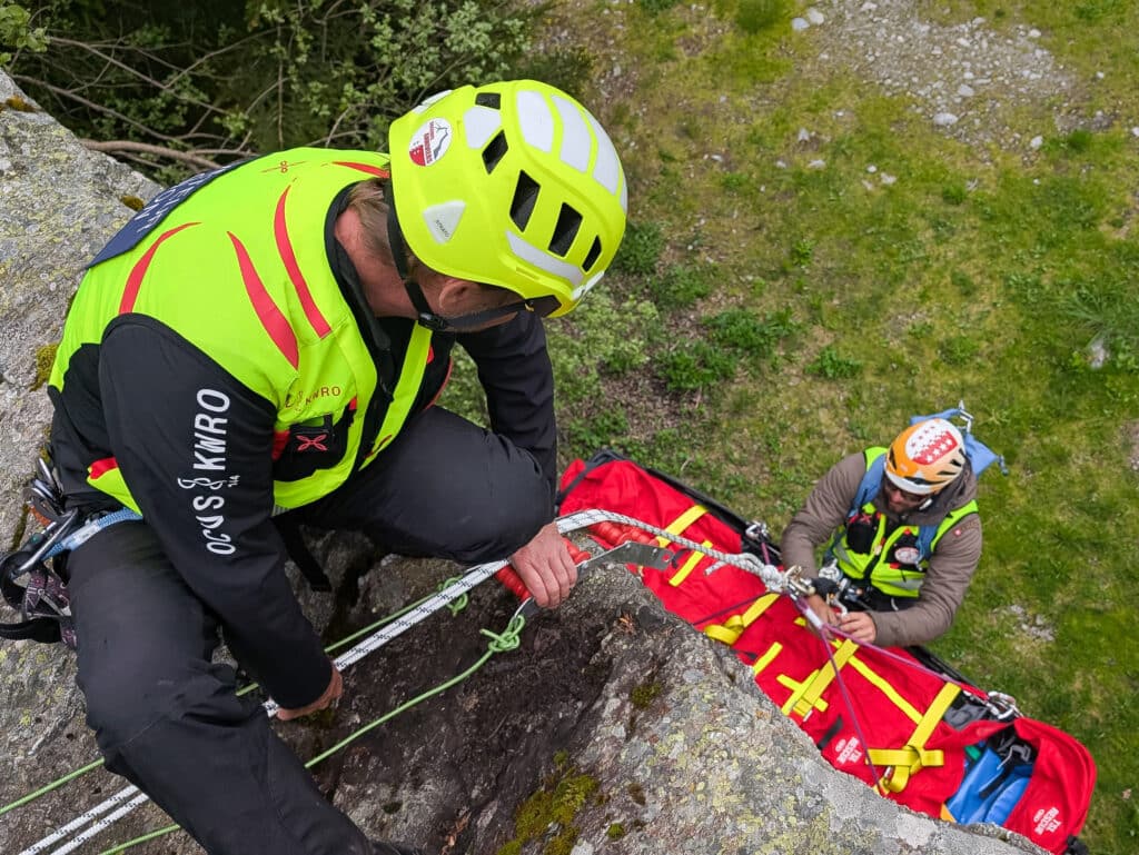 Deux secouristes en montagne avec civière et cordes.
