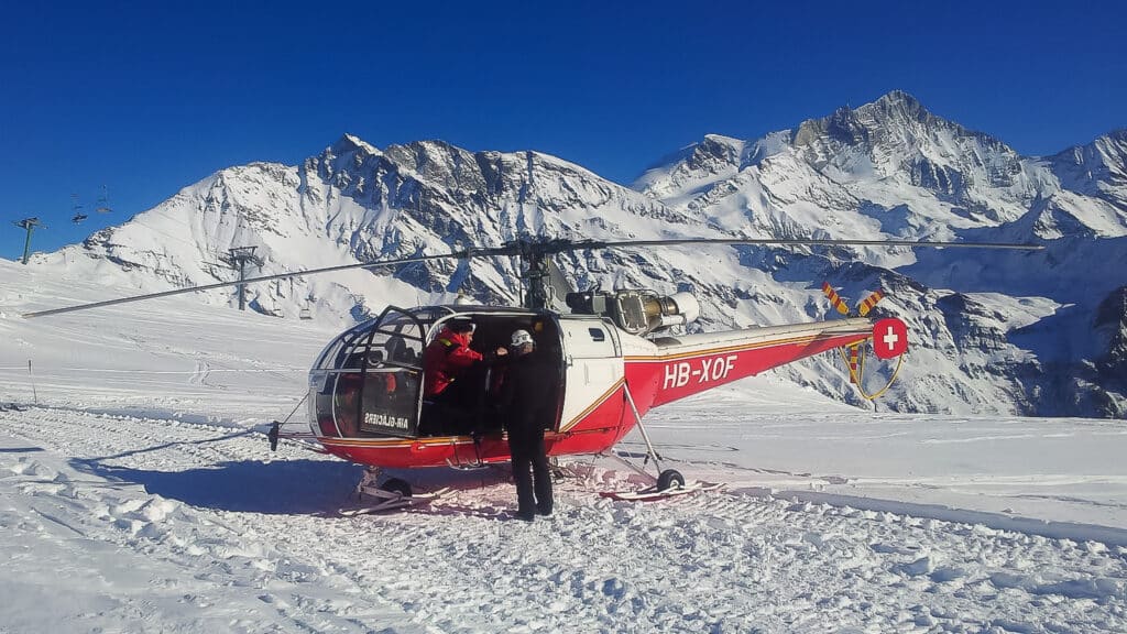 Hélicoptère rouge sur neige, montagnes suisses en arrière-plan.