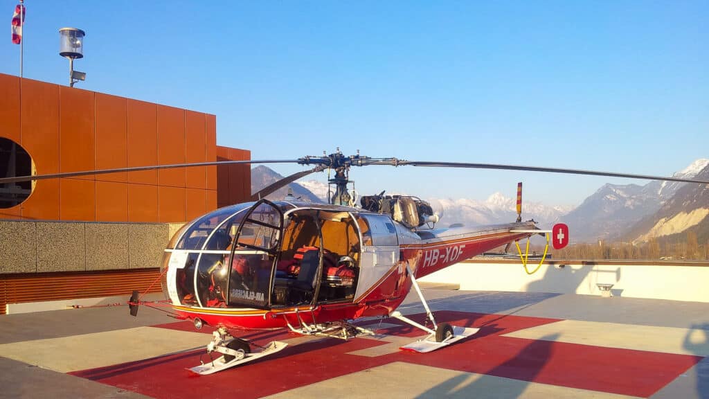 Hélicoptère rouge sur héliport de toit, montagnes enneigées.