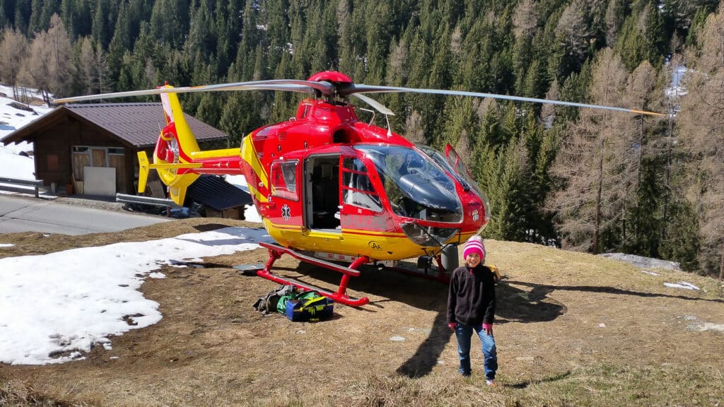 Hélicoptère de secours rouge et enfant en paysage montagneux enneigé.