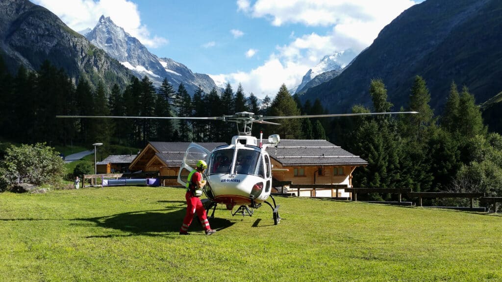 Secouriste et hélicoptère Air-Glaciers devant des montagnes enneigées.