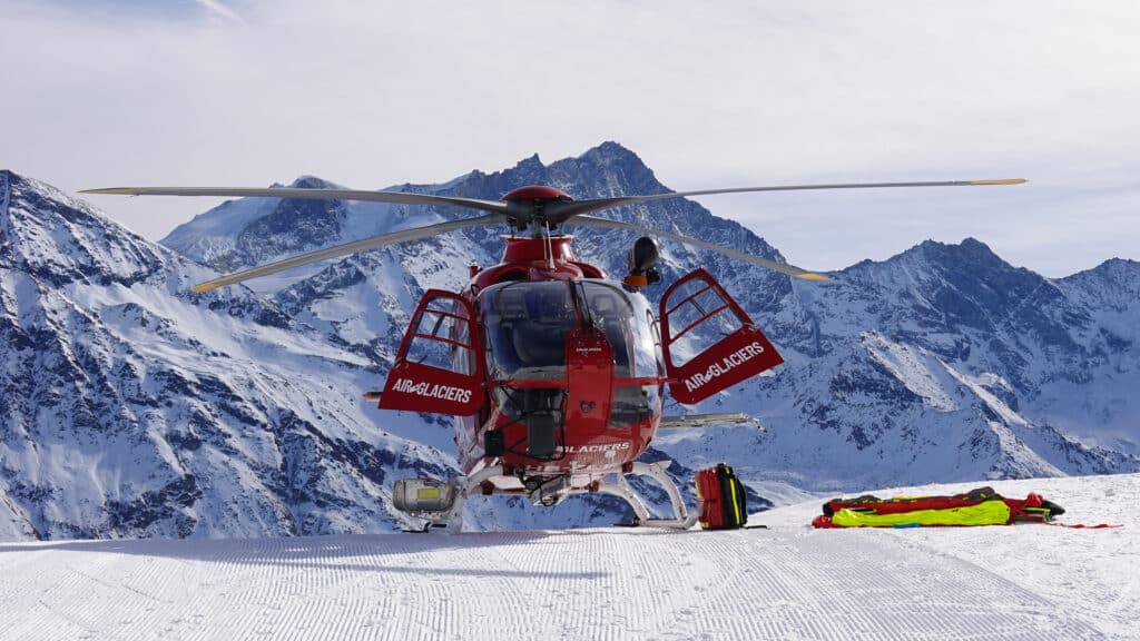Hélicoptère de secours AIR-GLACIERS posé sur neige en montagne.