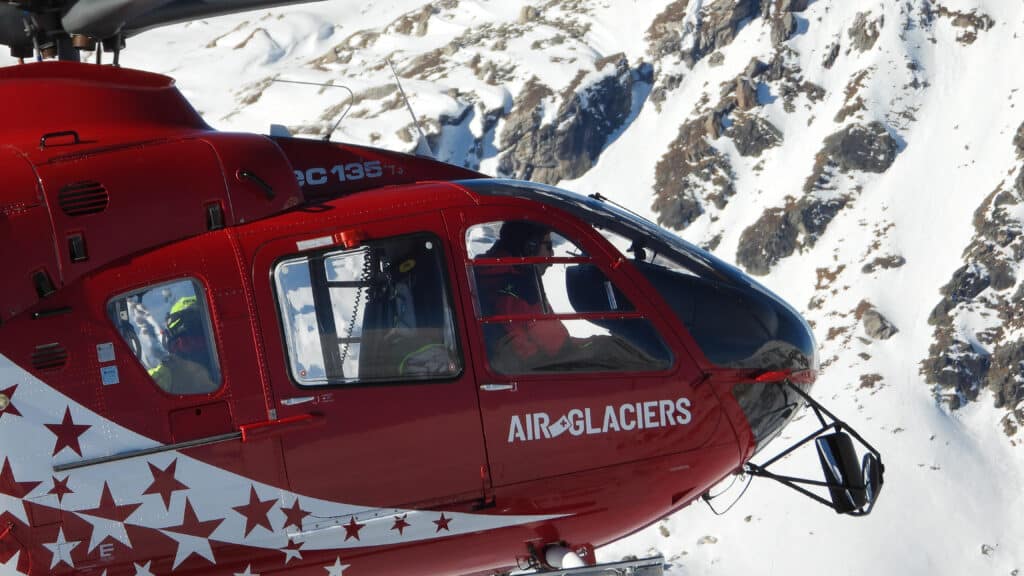 Hélicoptère rouge Air Glaciers en vol, montagnes enneigées.