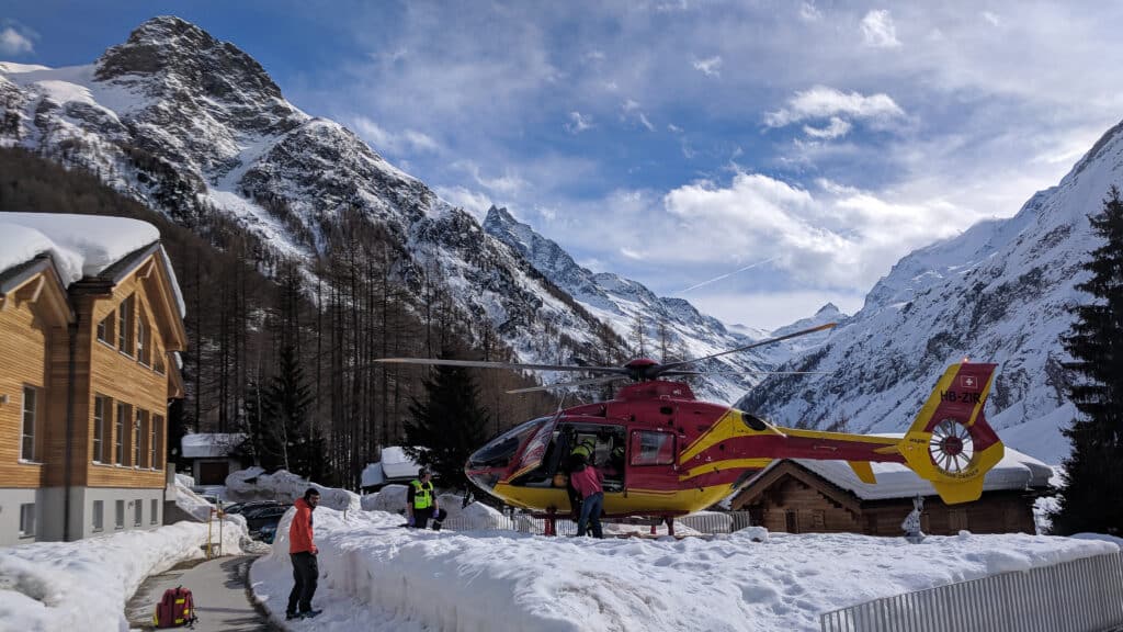 Hélicoptère rouge et jaune Air-Glaciers dans un paysage montagnard enneigé.