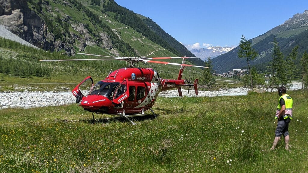 Hélicoptère rouge Air Zermatt posé dans une vallée alpine ensoleillée.