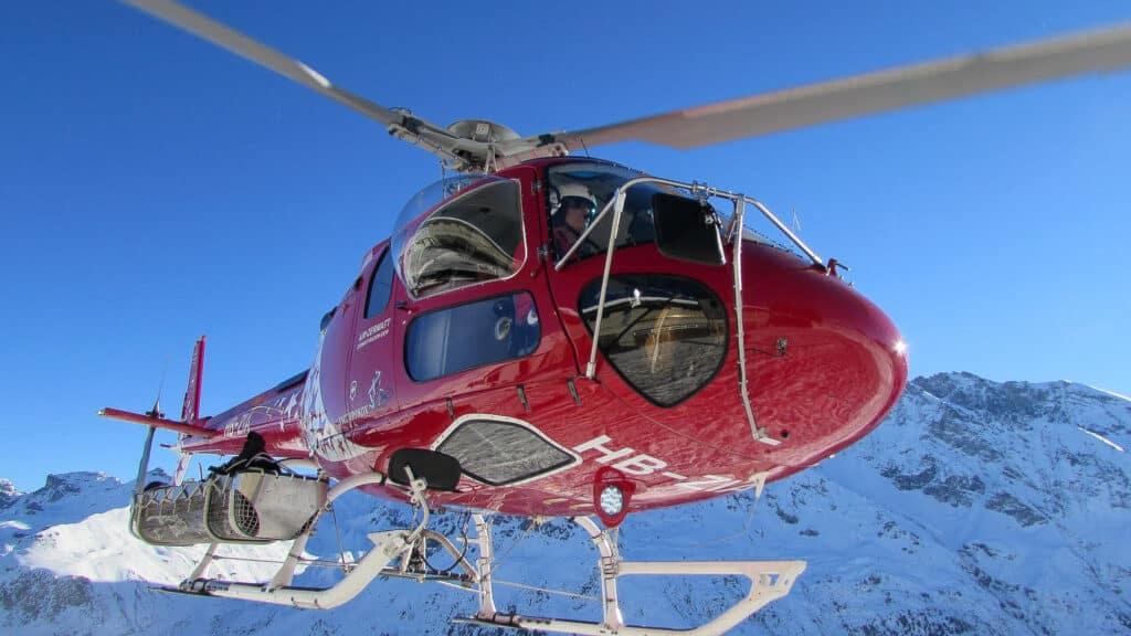 Hélicoptère rouge Air-Zermatt volant au-dessus de montagnes enneigées.