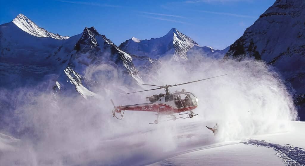 Hélicoptère au-dessus de la neige, soulève poudreuse, avec skieur.