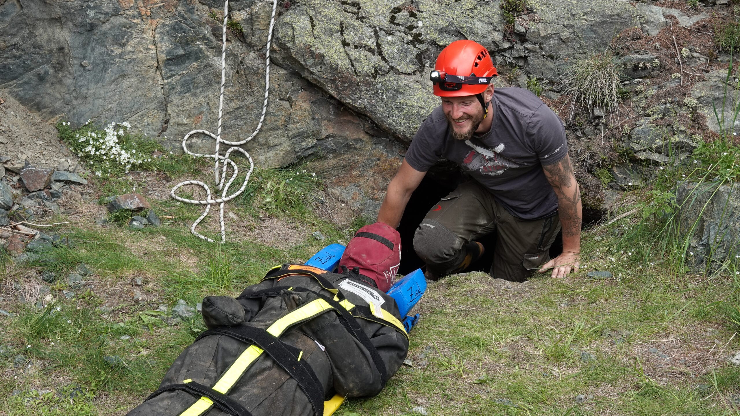 Spéléologue aidant un brancard à l'entrée d'une grotte rocheuse.