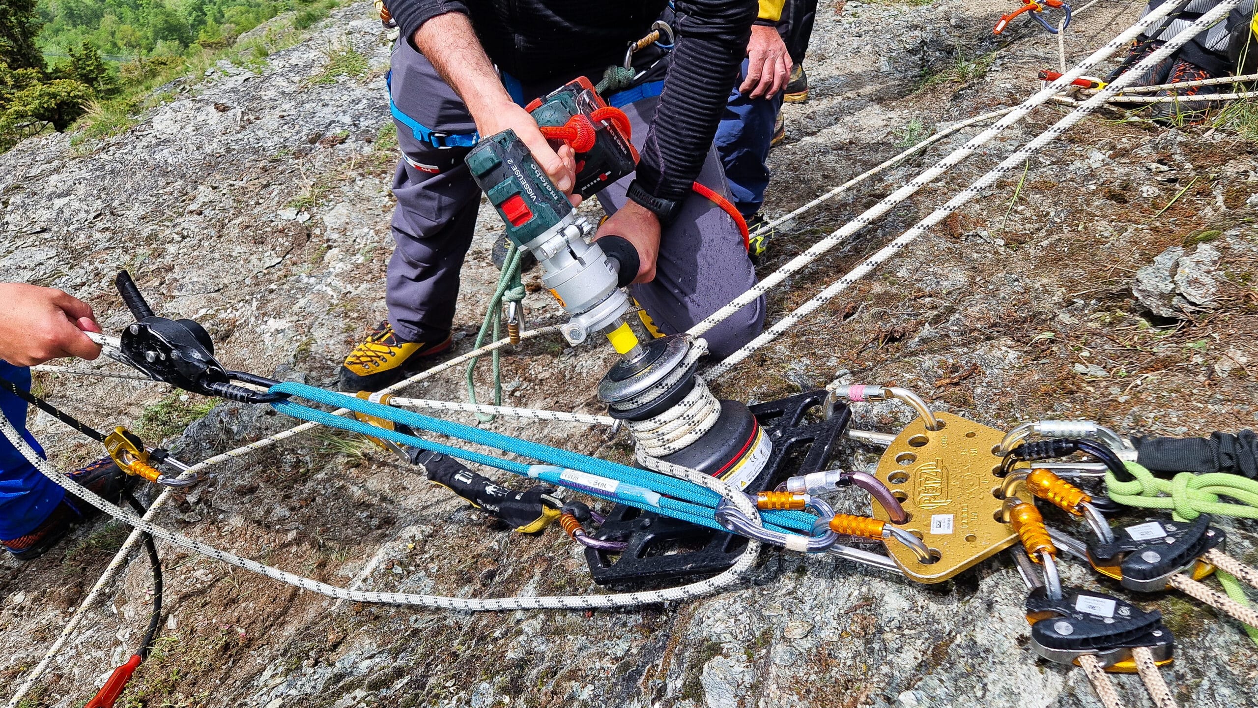 Homme utilisant une perceuse sur système de cordes Petzl en montagne.