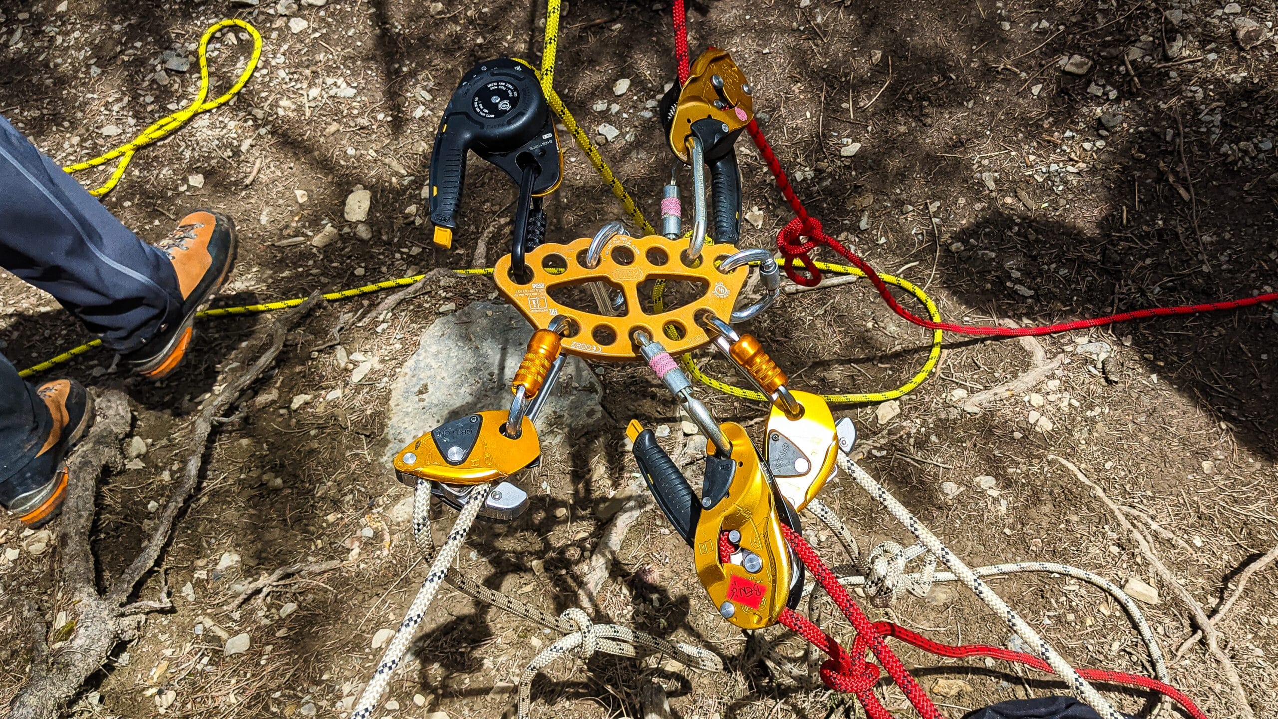 Platine, descendeurs Petzl et cordes sur sol terreux.