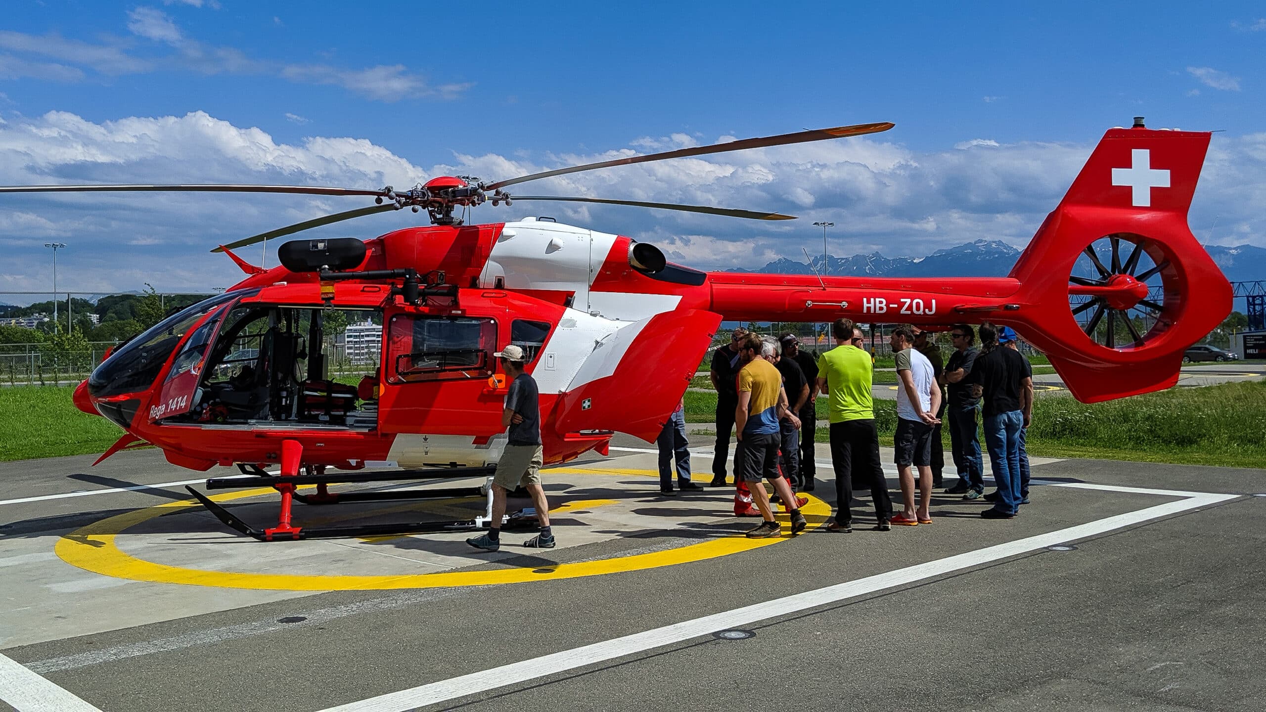 Hélicoptère REGA suisse rouge et blanc avec personnes et montagnes.
