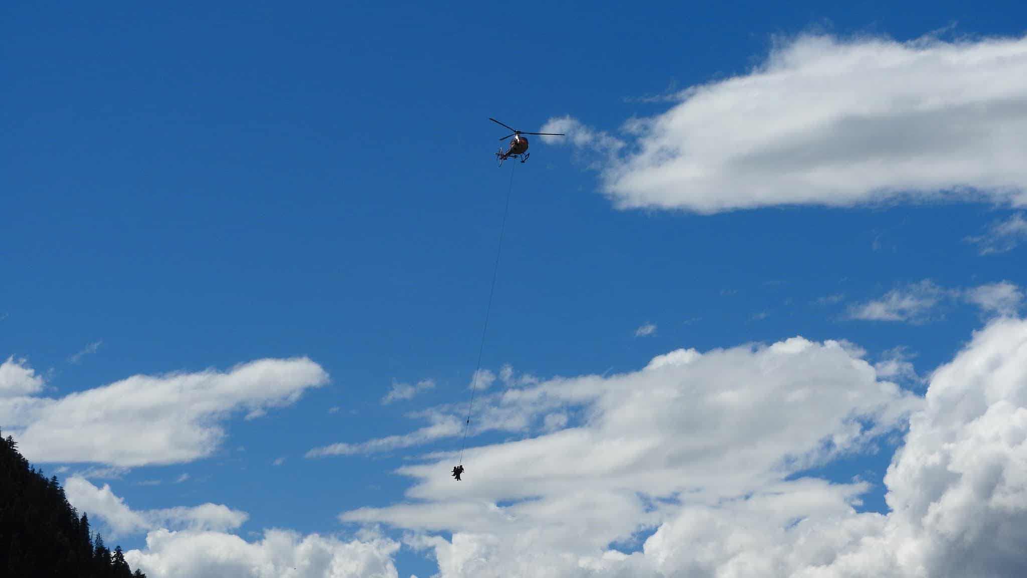 Hélicoptère de secours hélitreuillant une personne sous ciel bleu.