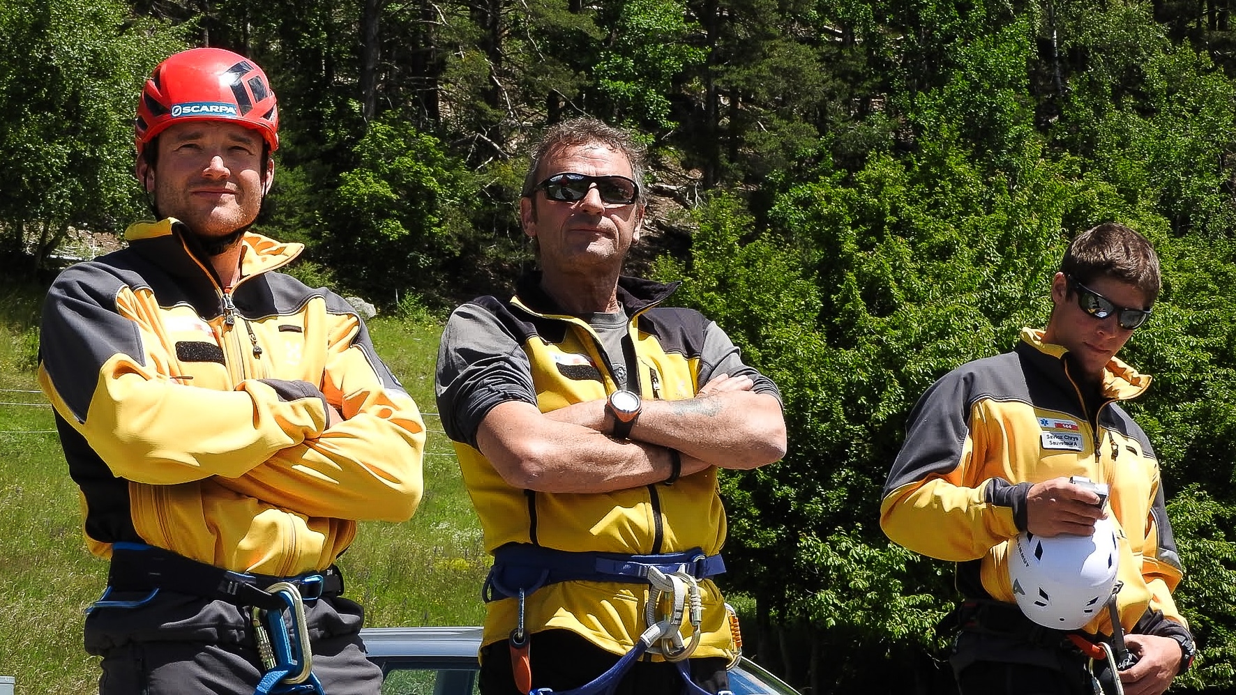 Trois hommes en équipement de montagne devant une forêt.