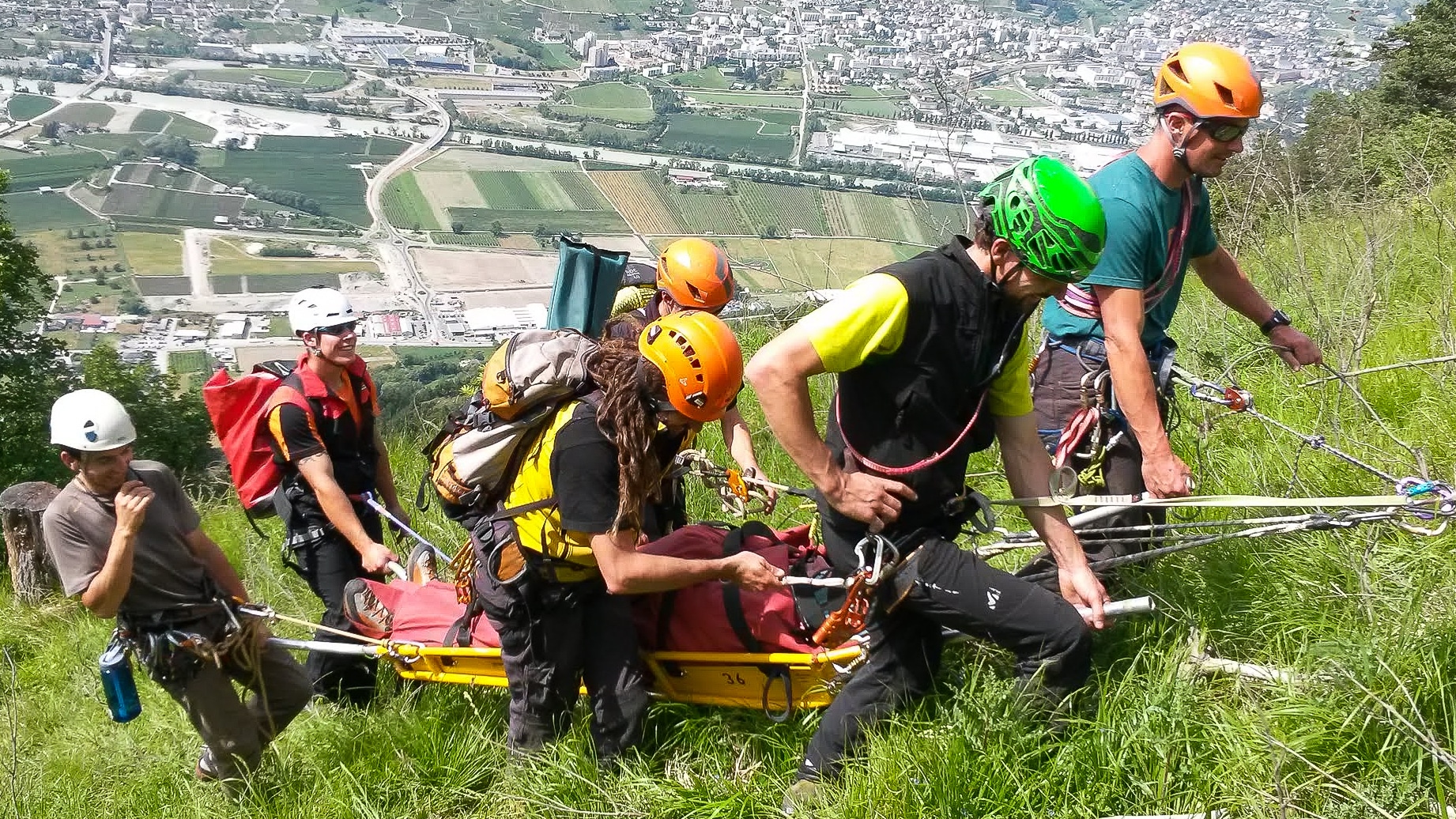 Entraînement au sauvetage en montagne avec civière sur une pente verdoyante.