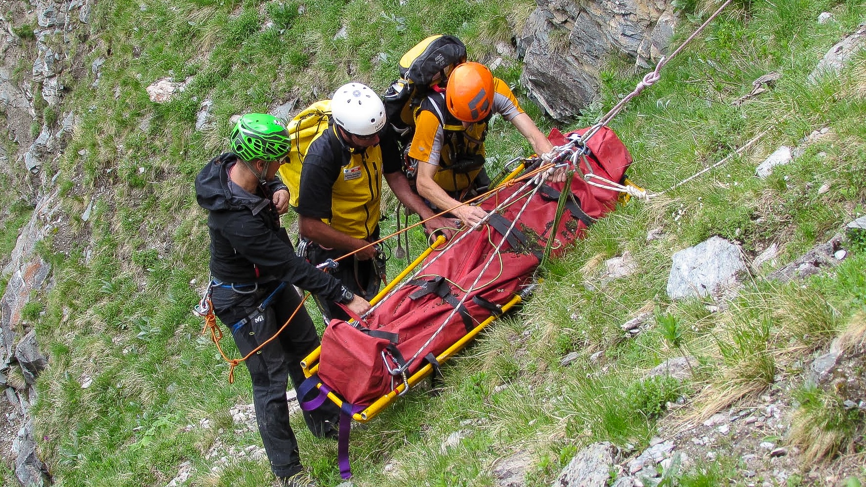 Sauvetage en montagne: trois secouristes manipulent un brancard rouge.