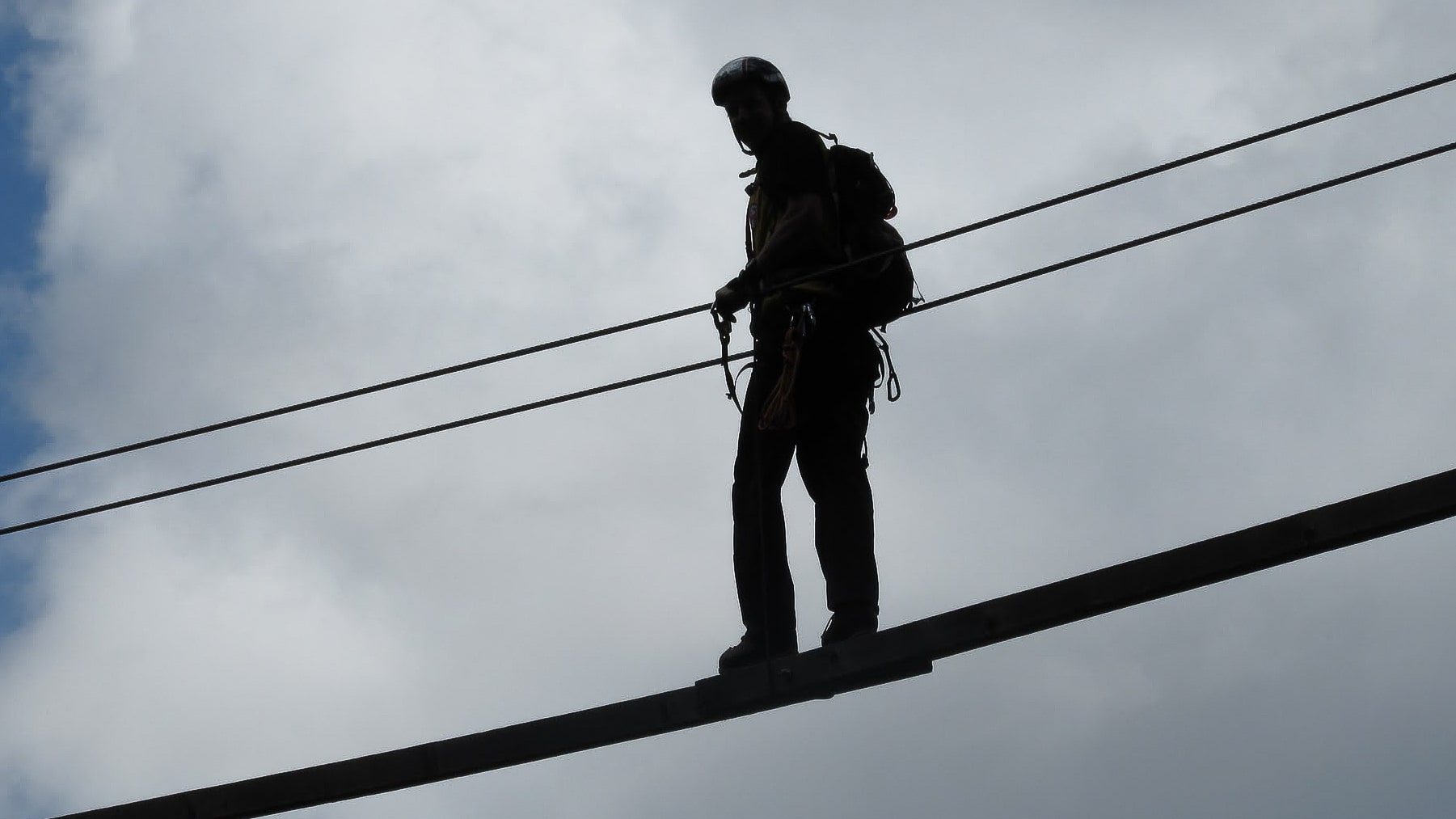 Silhouette d'un aventurier sur un parcours accrobranche sous ciel nuageux.