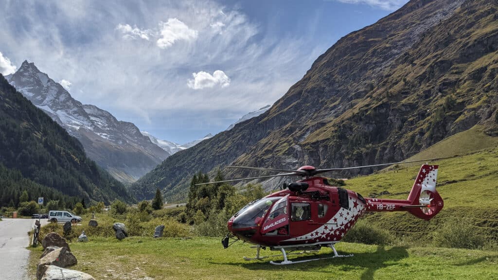 Hélicoptère rouge Air-Glaciers dans une vallée alpine enneigée.