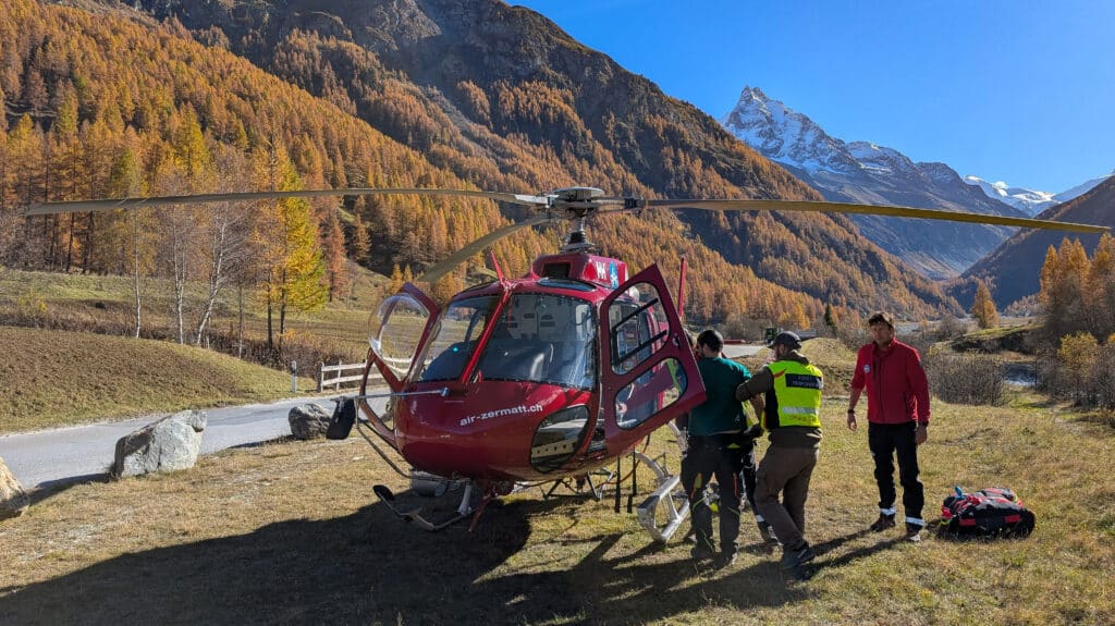 Hélicoptère Air Zermatt, secouristes assistent un patient en montagne automnale.