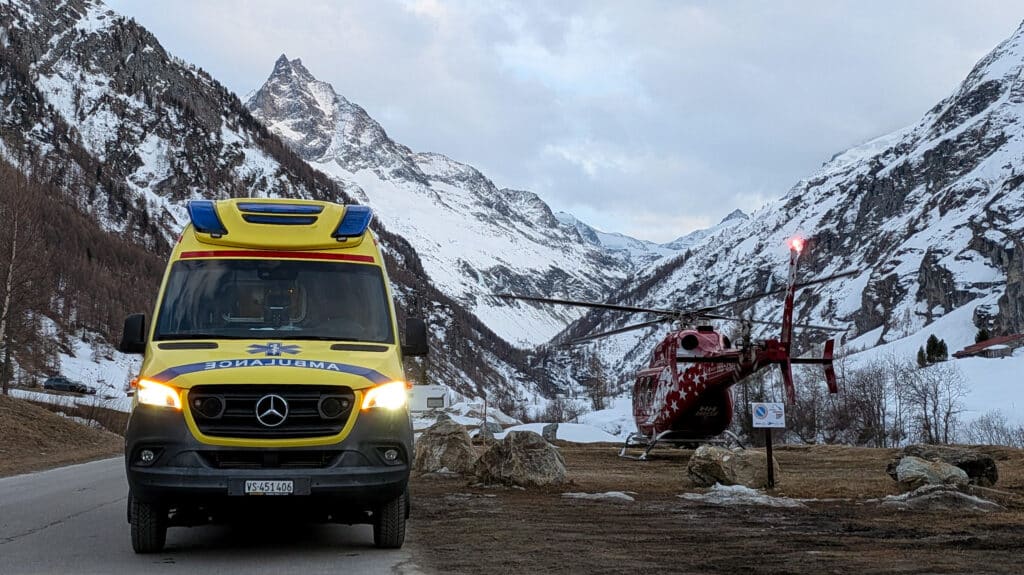 Ambulance et hélicoptère de sauvetage devant des montagnes enneigées.